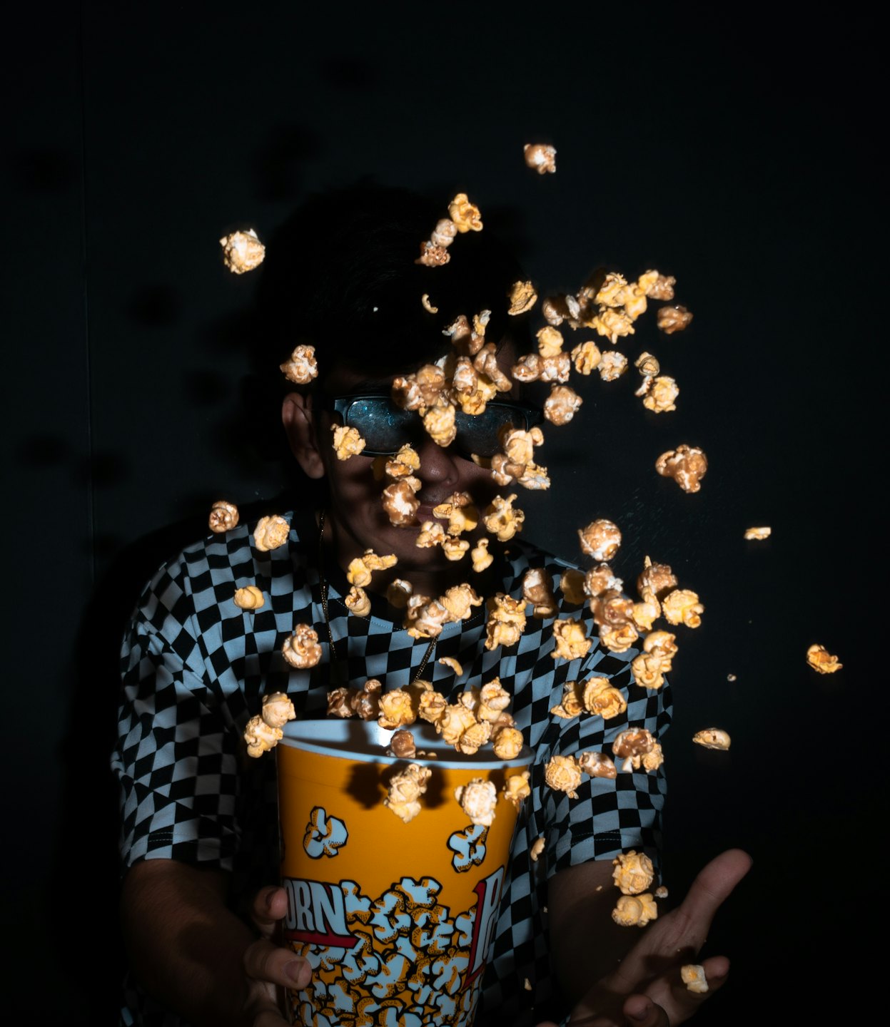 Young adult with 3D glasses holds popcorn bucket with flying popcorn.