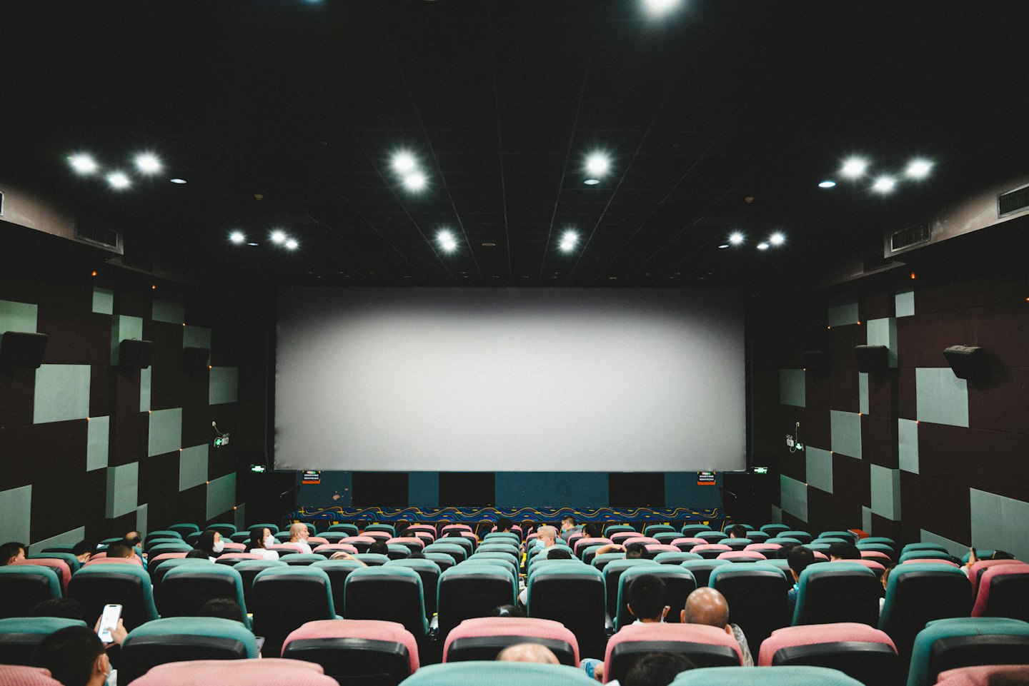 Audience members sit in colorful seats facing a blank screen.