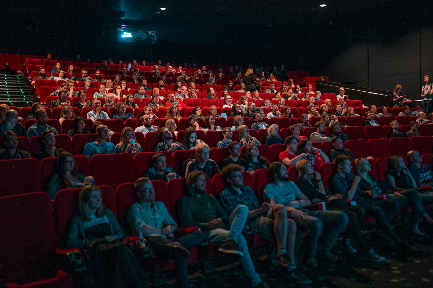 Adults watch a movie in a crowded, dimly lit theater.