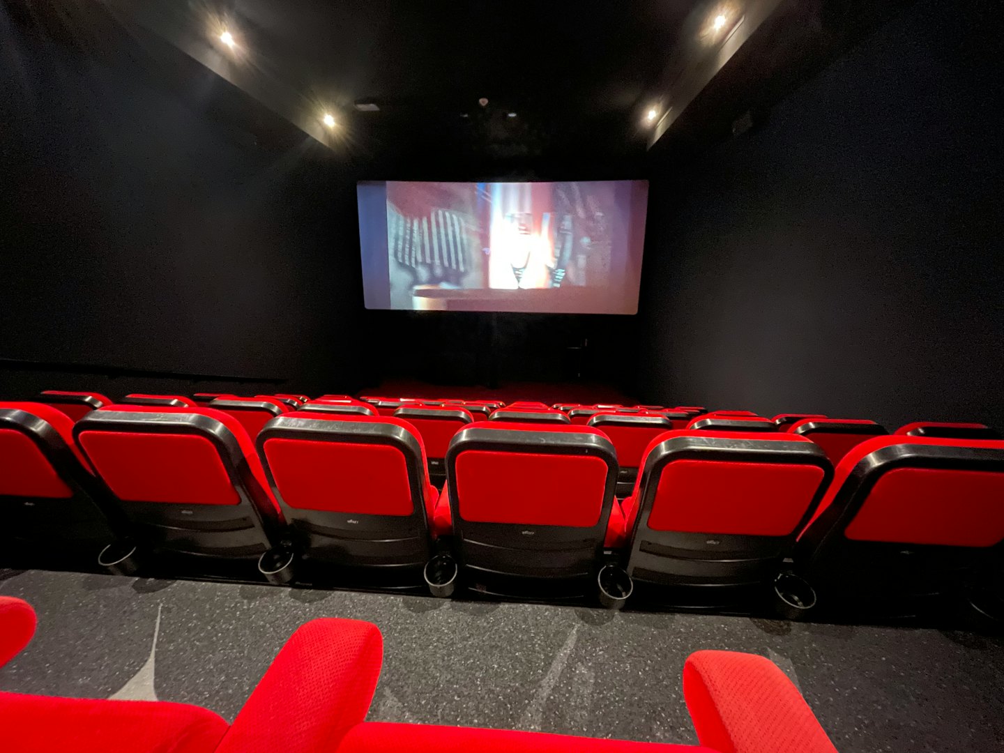 Empty movie theater with red seats and screen playing a film.